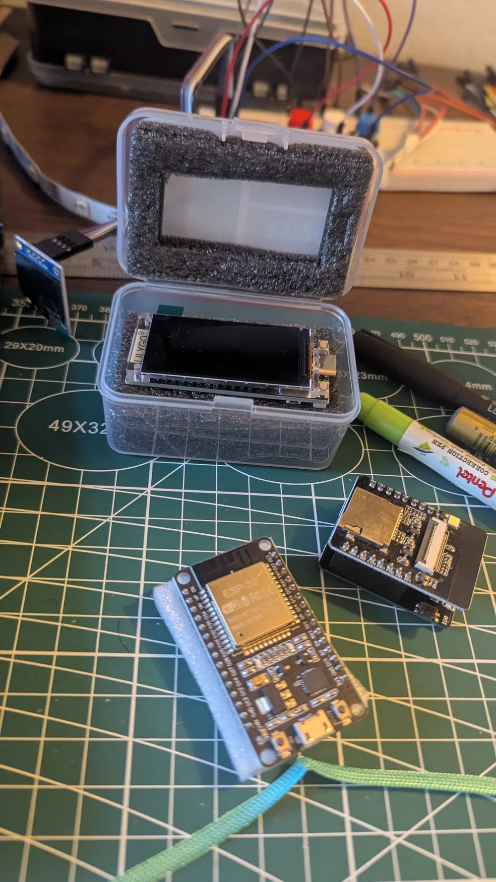 A small display in a foam-lined plastic case with ESP32 boards on the workbench