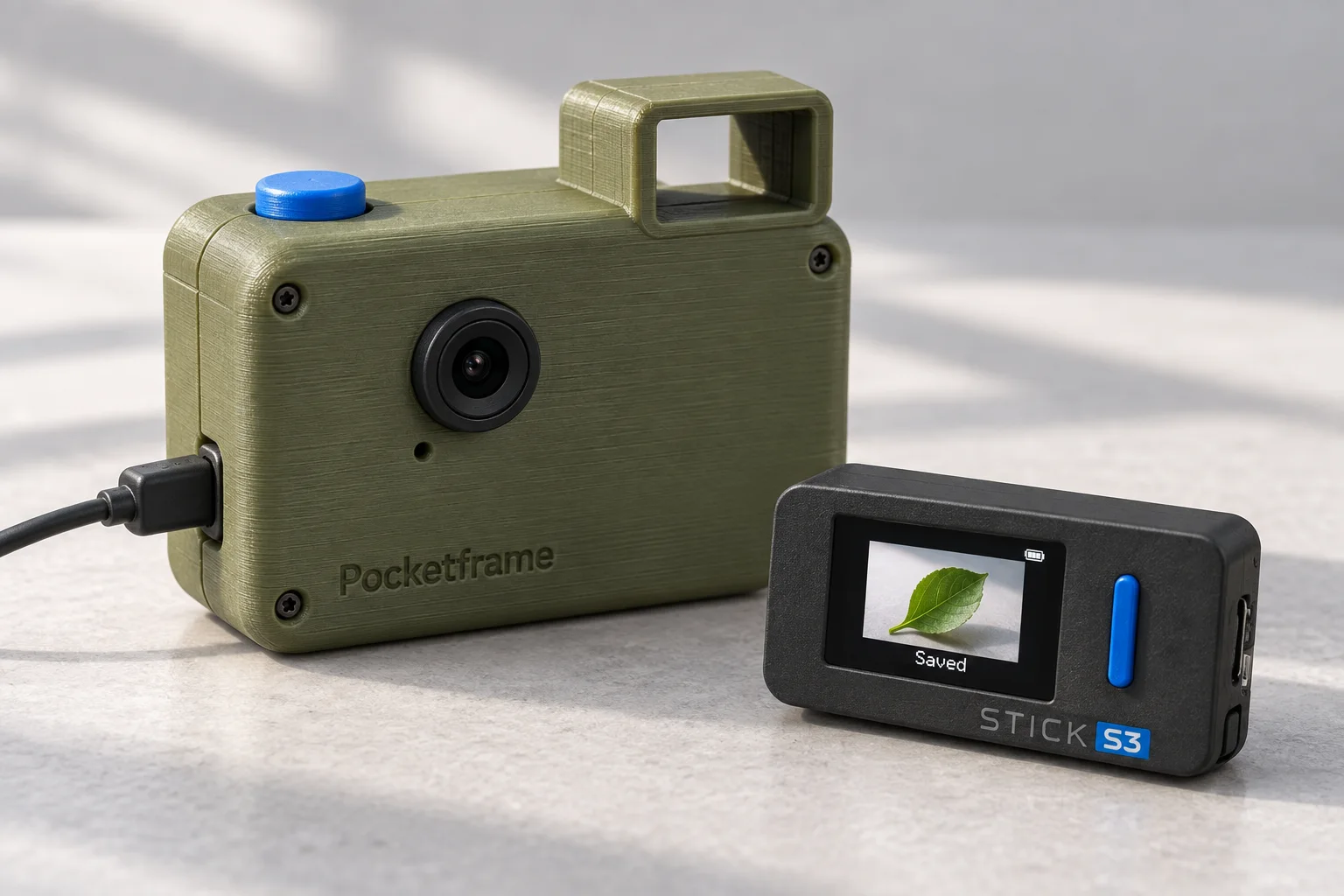 AI concept render of an olive printed Pocketframe camera with a blue shutter and open viewfinder, beside a black StickS3 remote showing a leaf photograph