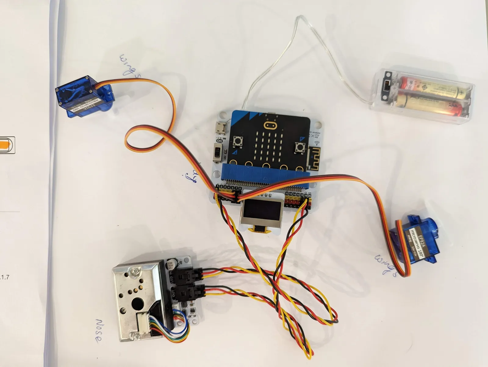 A micro:bit connected to motors, a battery and wiring on a project table