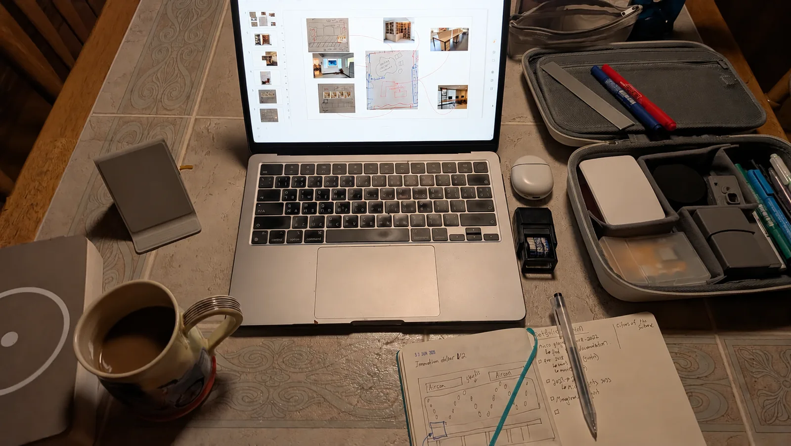 A laptop showing an atelier moodboard beside notebook layout sketches, pens and making tools